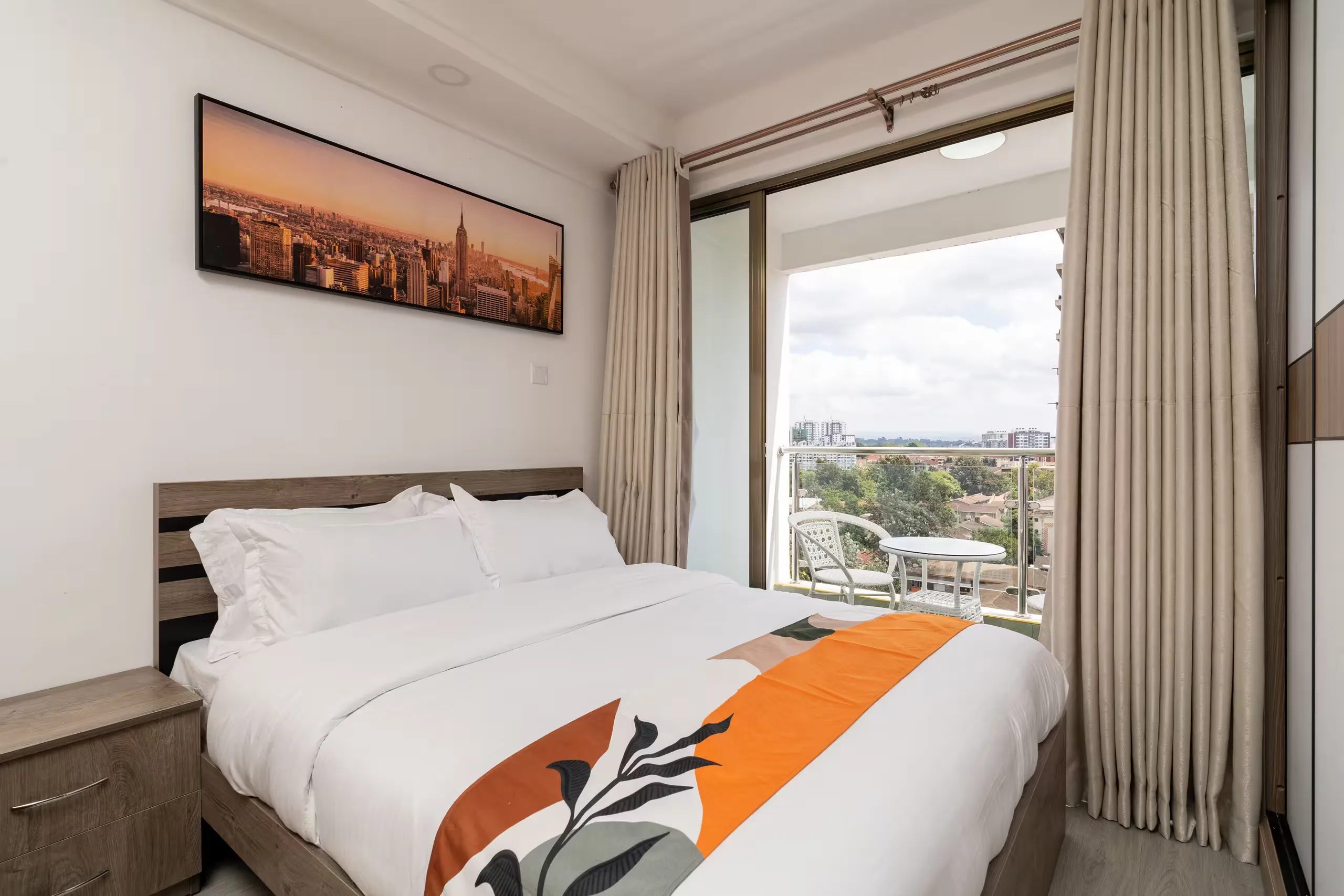 Bed with white linens and an orange runner beside balcony doors